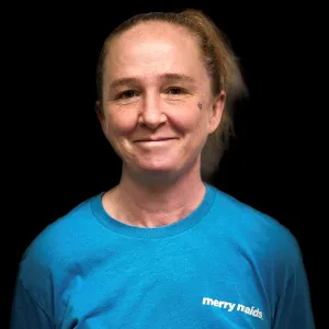woman with blonde hair wearing a blue merry maids tshirt standing in front of a black photo backdrop